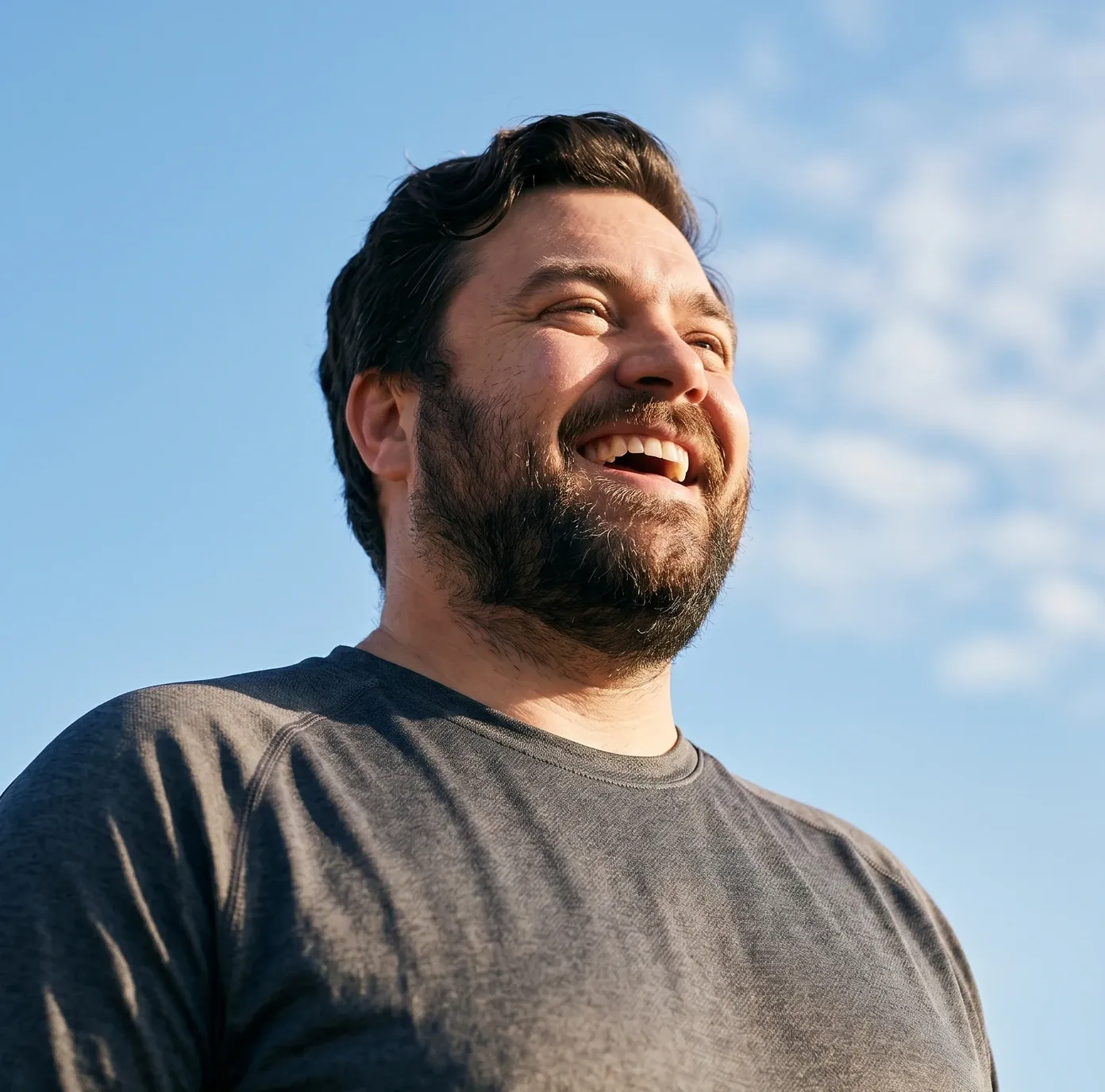 Lachender Mann mit Bart vor blauem Himmel